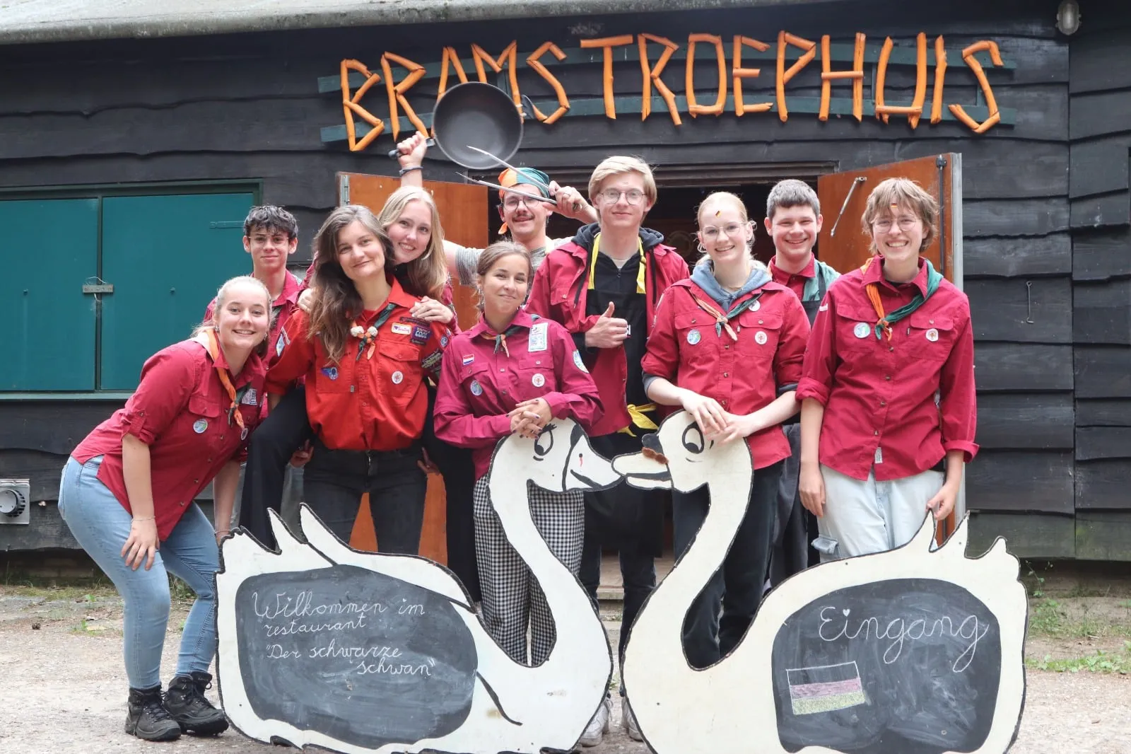 Leiding in rode blouses bij het bord Brams Troephuis met twee houten zwanen