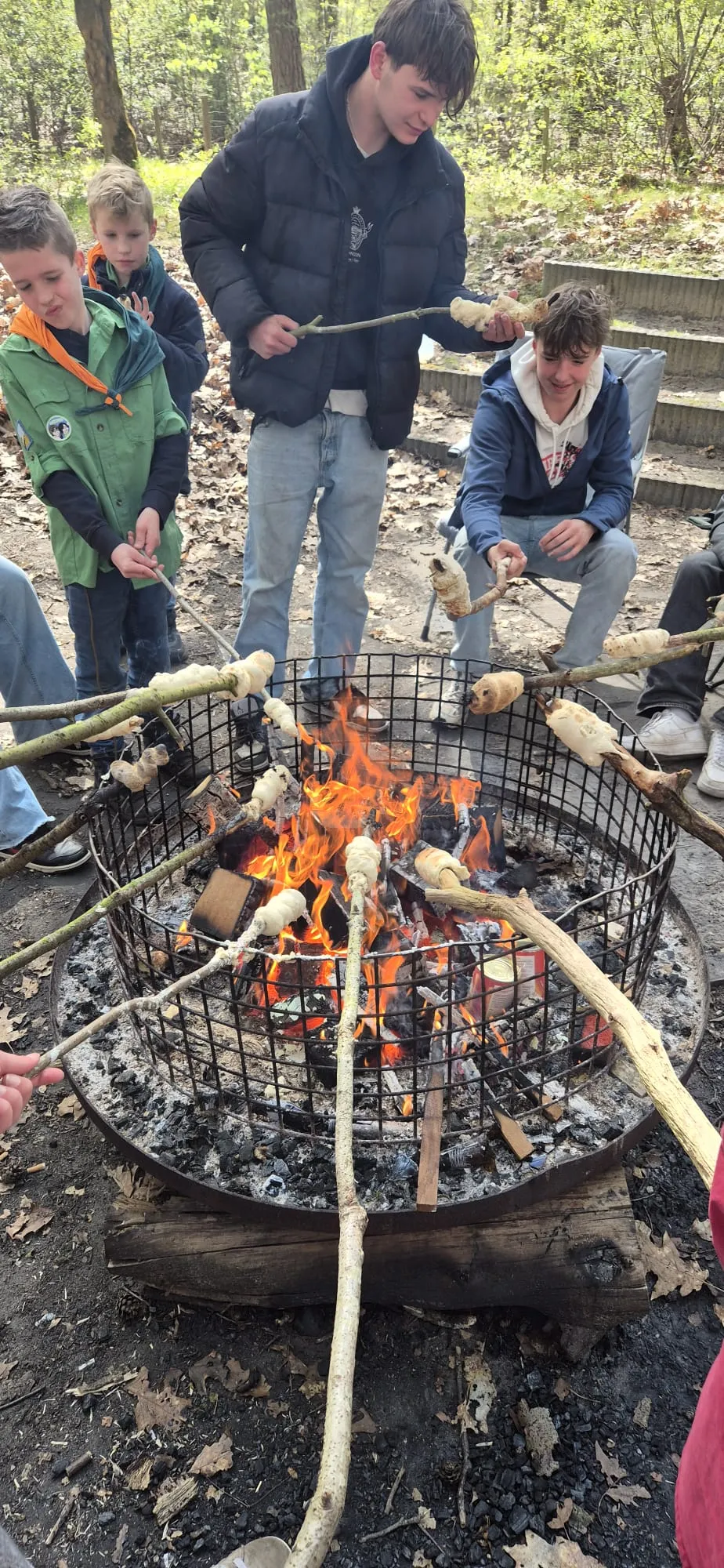 Welpen en explorers bakken broodjes aan stokken boven een vuurkorf