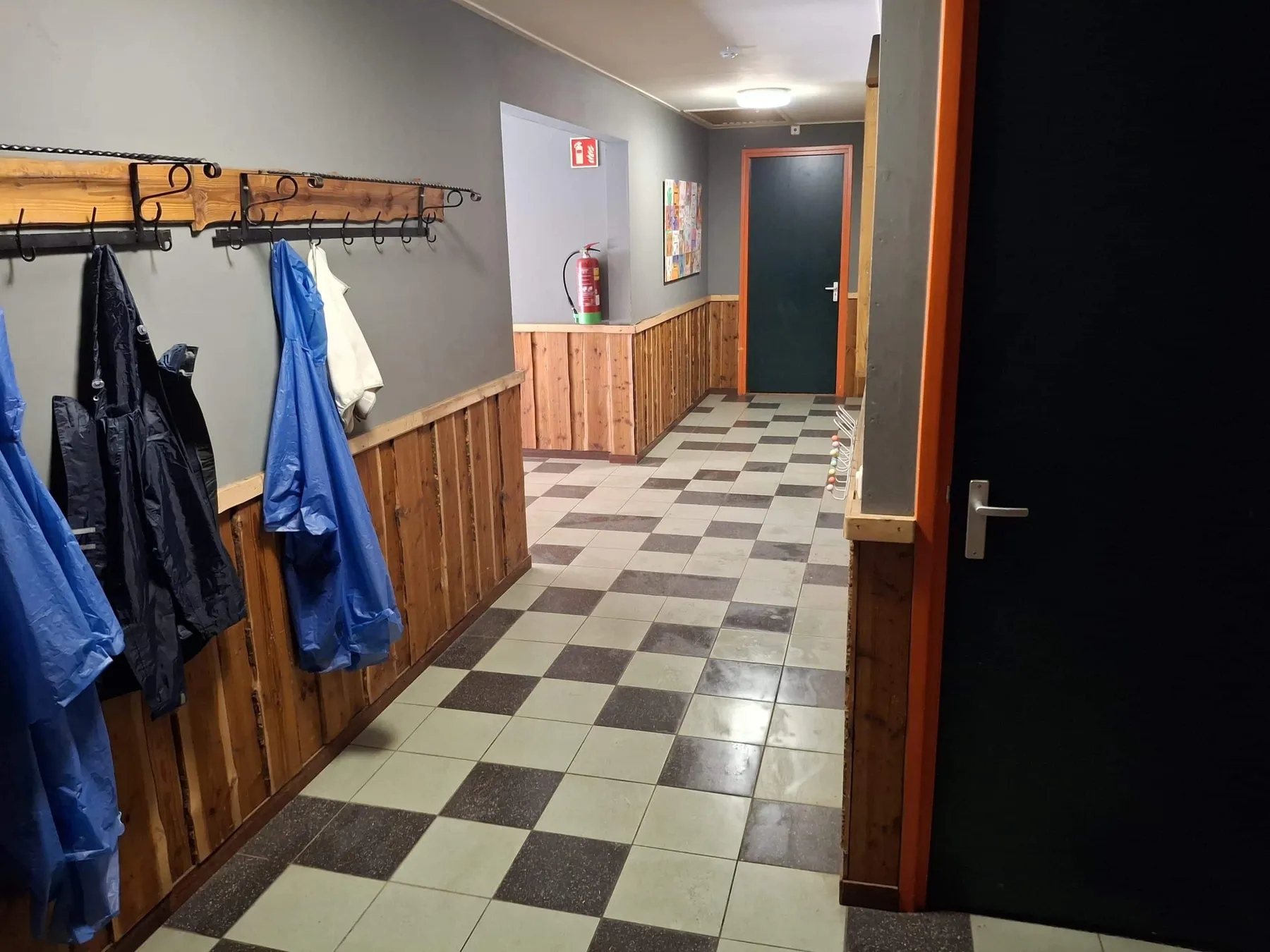 Gang met kapstokken vol jassen en een geblokte tegelvloer