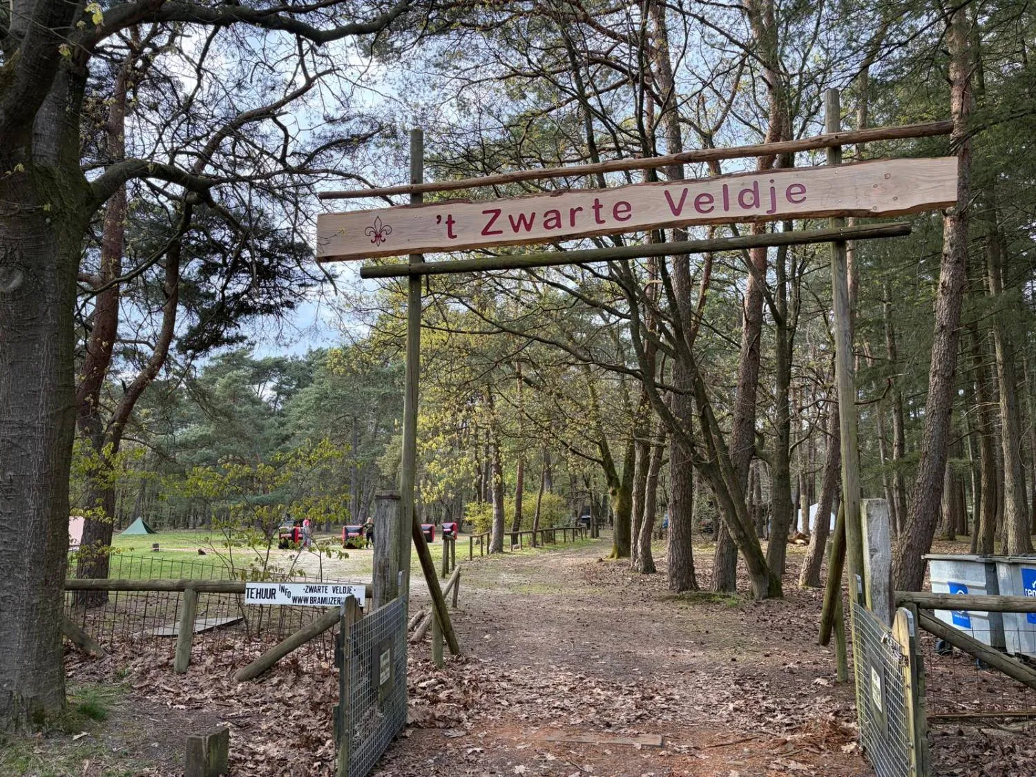 Houten toegangspoort met het bord 't Zwarte Veldje, met daarachter het kampeerveld tussen de bomen