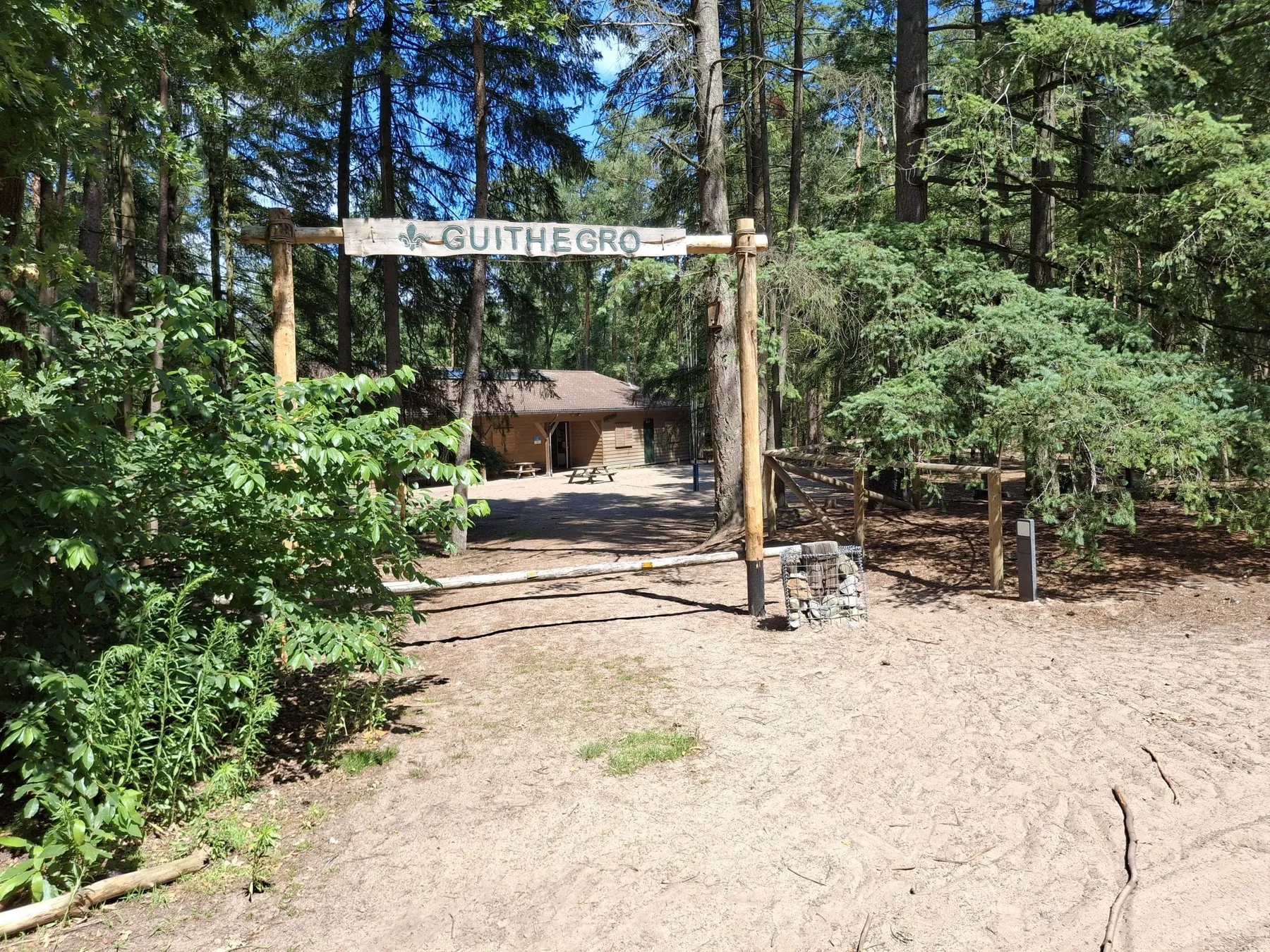 Houten toegangspoort met het bord Guithégro, met daarachter het clubhuis in het bos
