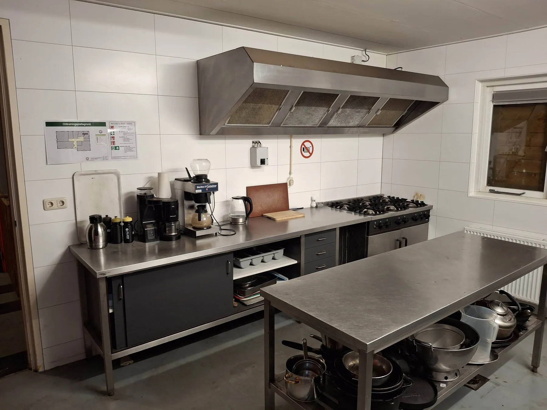 Professionele keuken met gasfornuis, afzuigkap, koffiezetapparaten en RVS werktafel