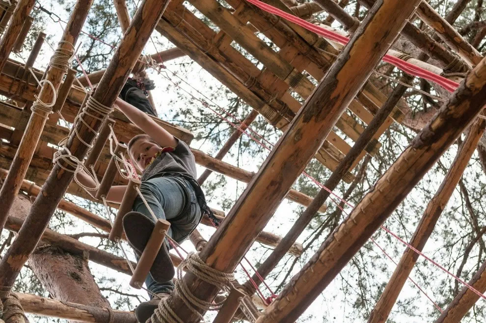 Een scout klimt door een zelfgebouwde pioniertoren van boomstammen en touw