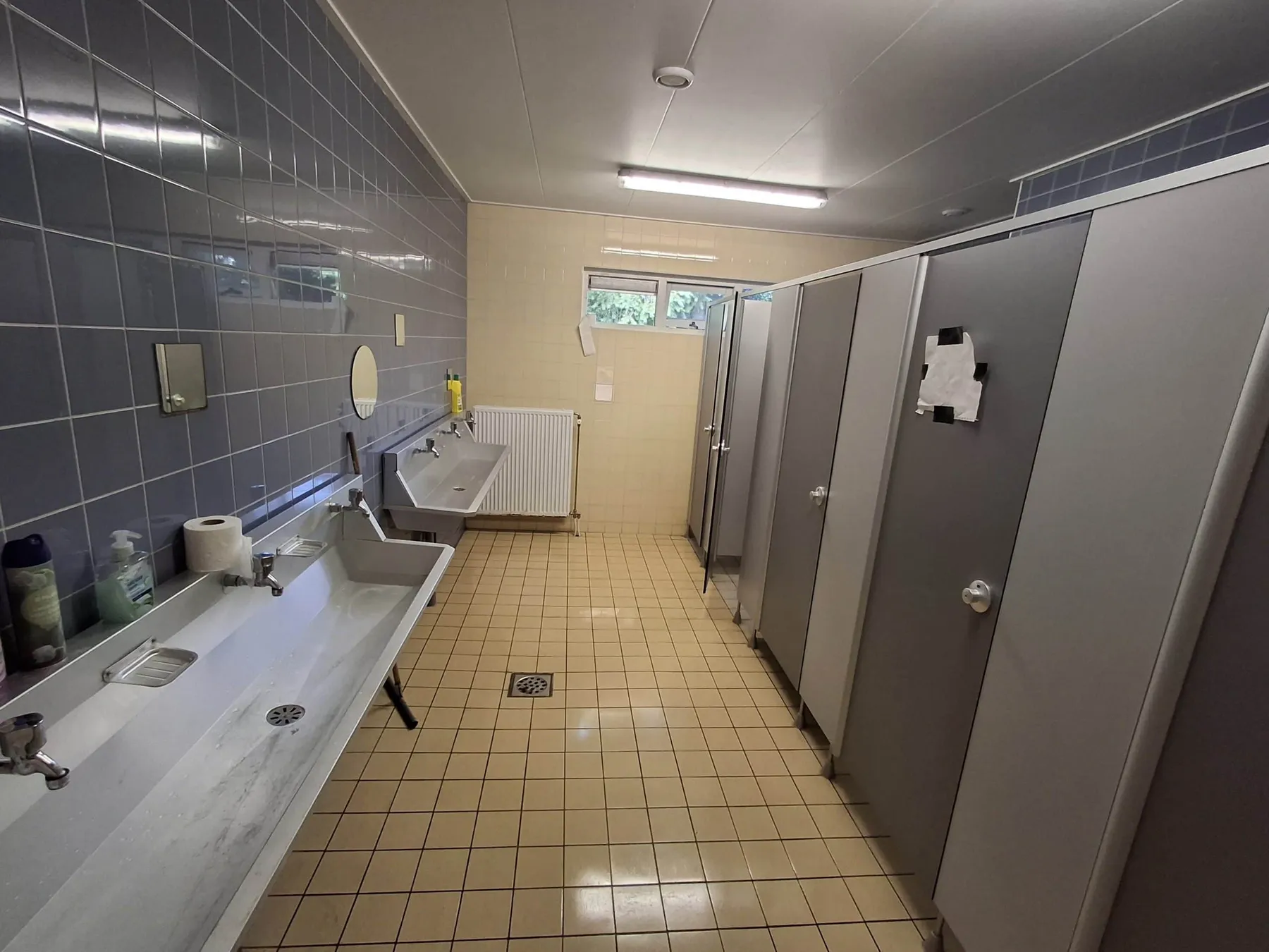 Sanitaire ruimte met lange wasbak met kranen en een rij toiletcabines