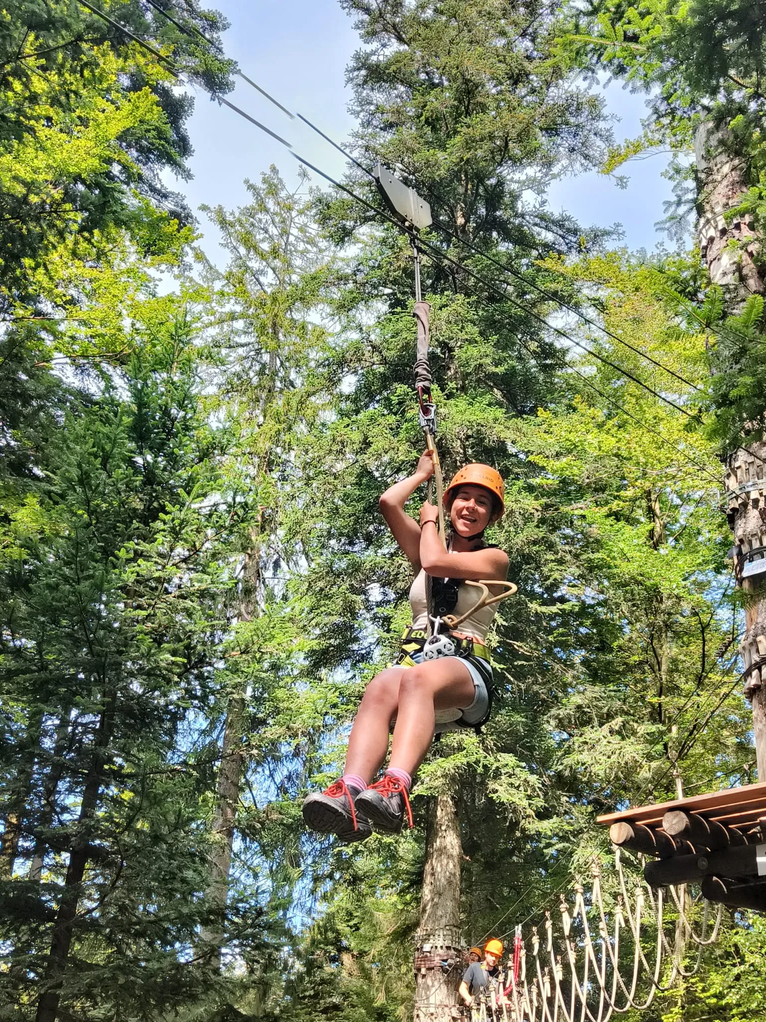 Een scout met helm glijdt aan een tokkelbaan tussen hoge bomen