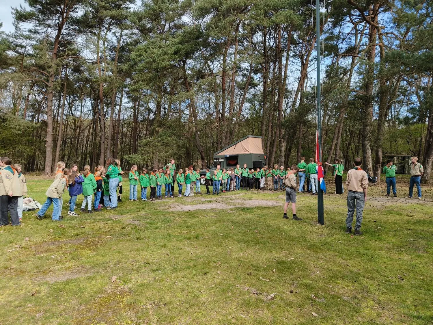 Alle speltakken staan in een grote kring rond de vlaggenmast op het veld in het bos