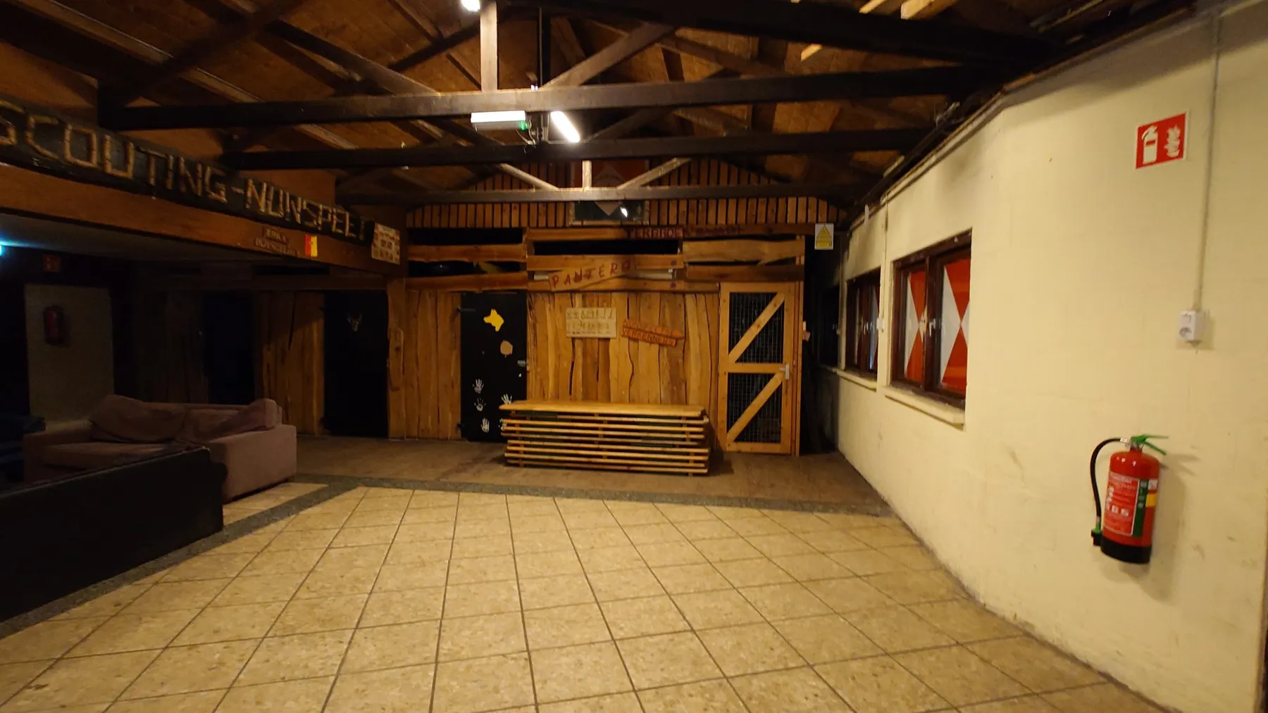 Grote zaal met houten balkenplafond en een verhoogd houten podium achterin